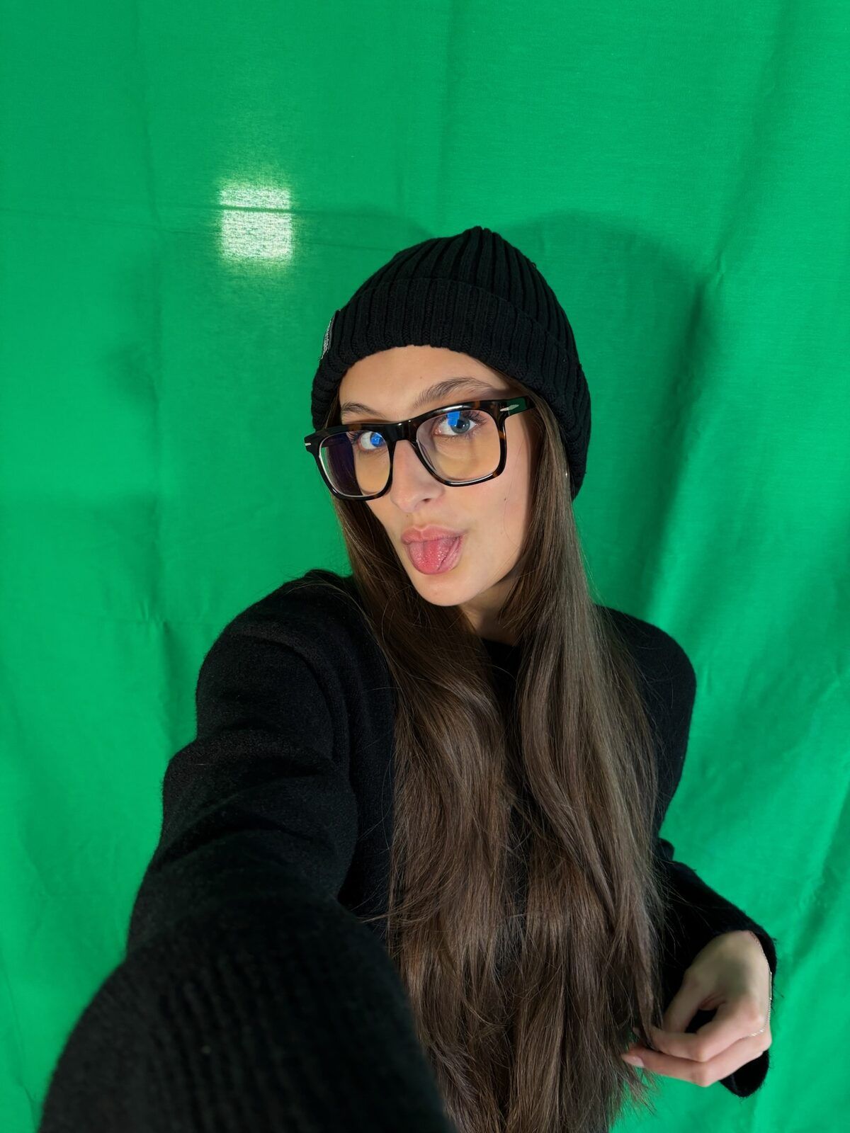 Lorena de Marco mit schwarzer Mütze und Brille vor einem Greenscreen