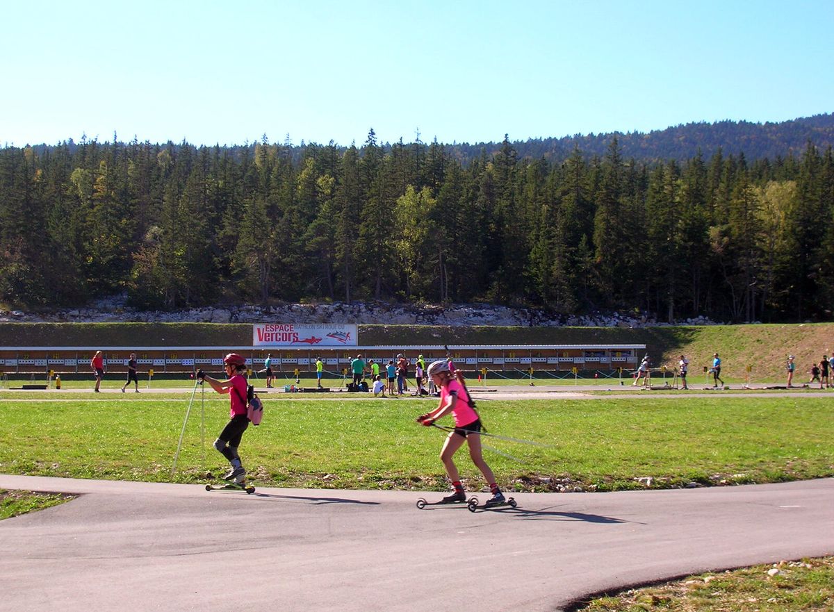 Zwei Sportlerinnen auf Skirollern vor der Scheibenreihe eines Biathlon-Schießstands