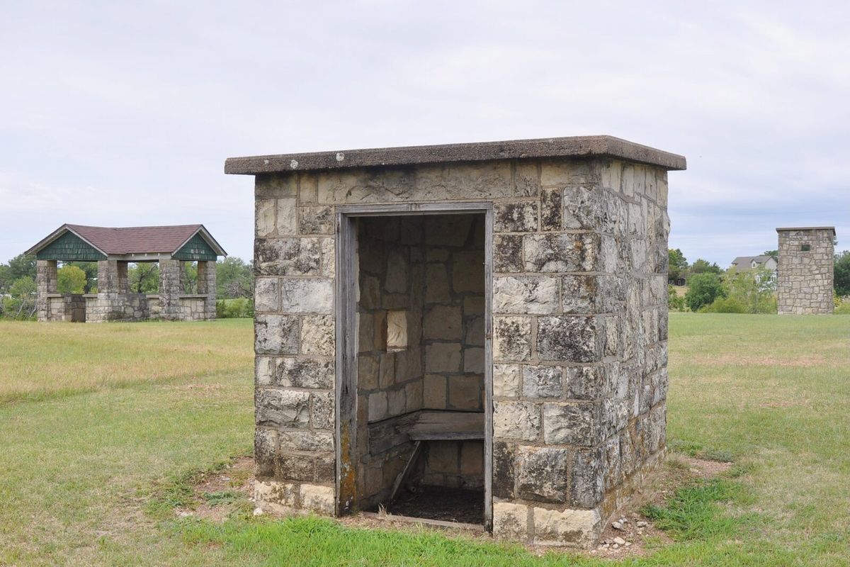 Steinernes Niederhaus eines Skeetstands auf einer Wiese, im Hintergrund links das Hochhaus