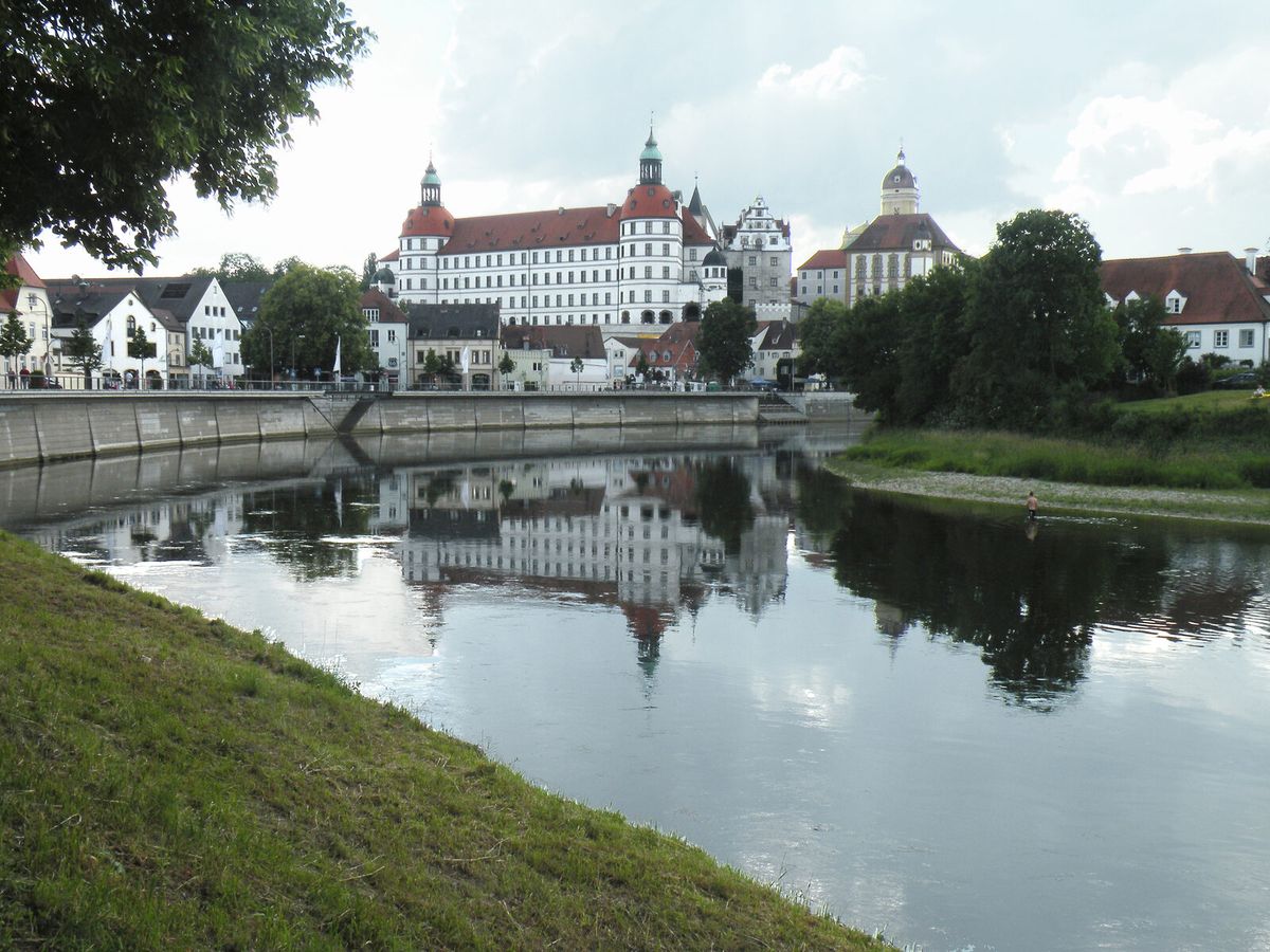 Das Neuburger Residenzschloss über der Donau, davor das bewaldete Flussufer