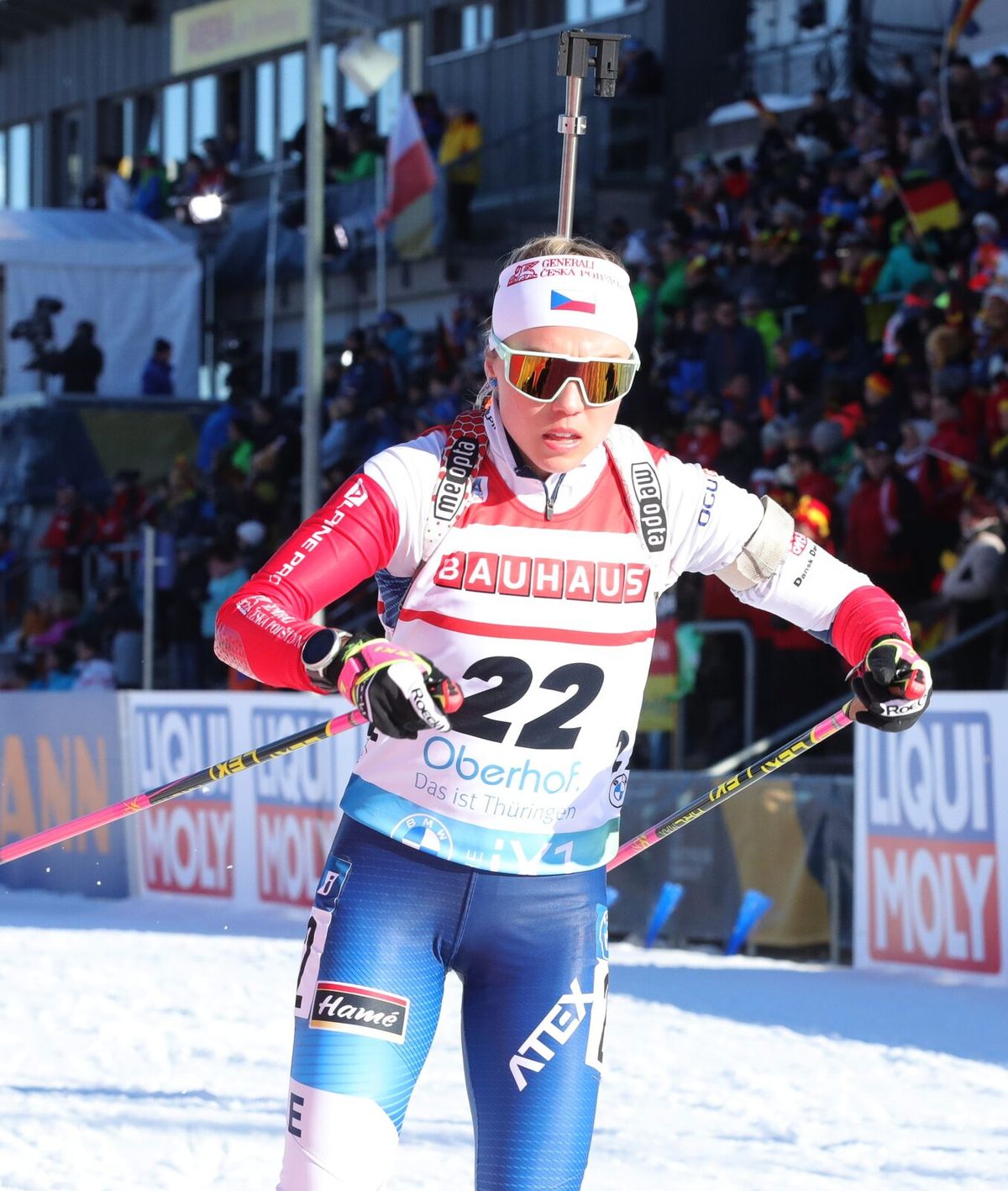 Biathletin mit Gewehr auf dem Rücken vor voller Tribüne