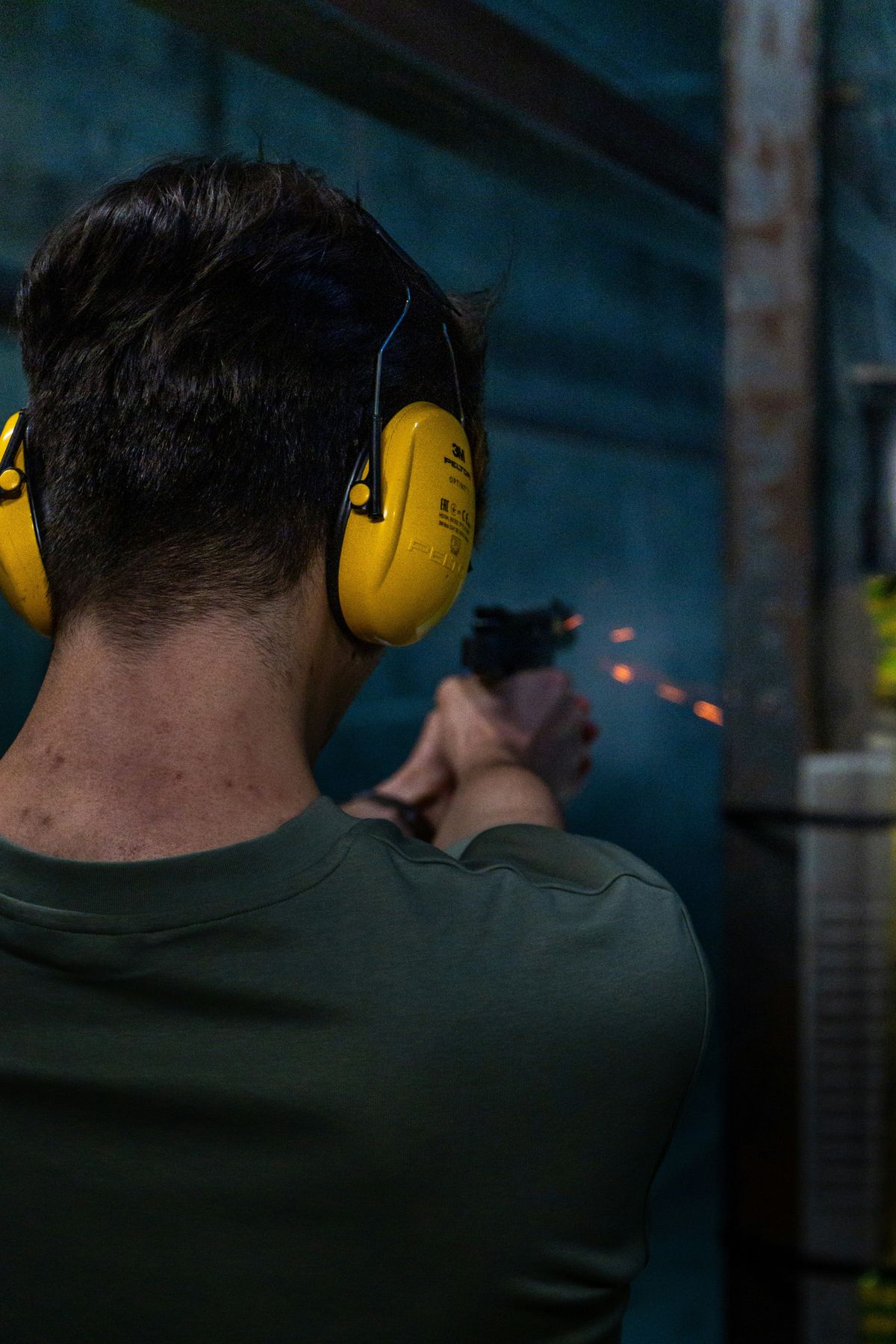 Person mit Gehörschutz schießt mit einer Kurzwaffe auf einem Indoor-Schießstand.