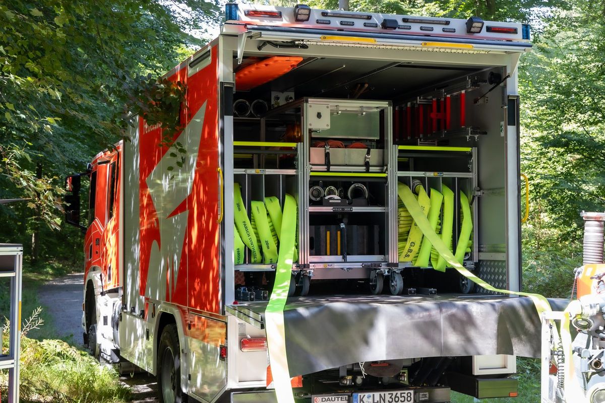 Logistik-Löschfahrzeug der Feuerwehr auf einem Waldweg beim Verlegen einer langen Schlauchleitung