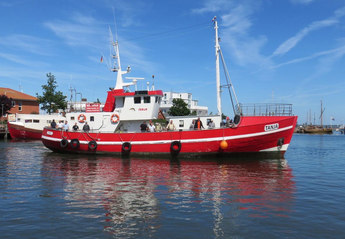 Roter Angelkutter MS TANJA läuft in einen Hafen ein, rund zwei Dutzend Angler stehen mit Ruten an der Reling