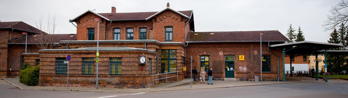 Backsteinernes Empfangsgebäude des Bahnhofs Parchim mit Vorplatz und Bahnhofsuhr