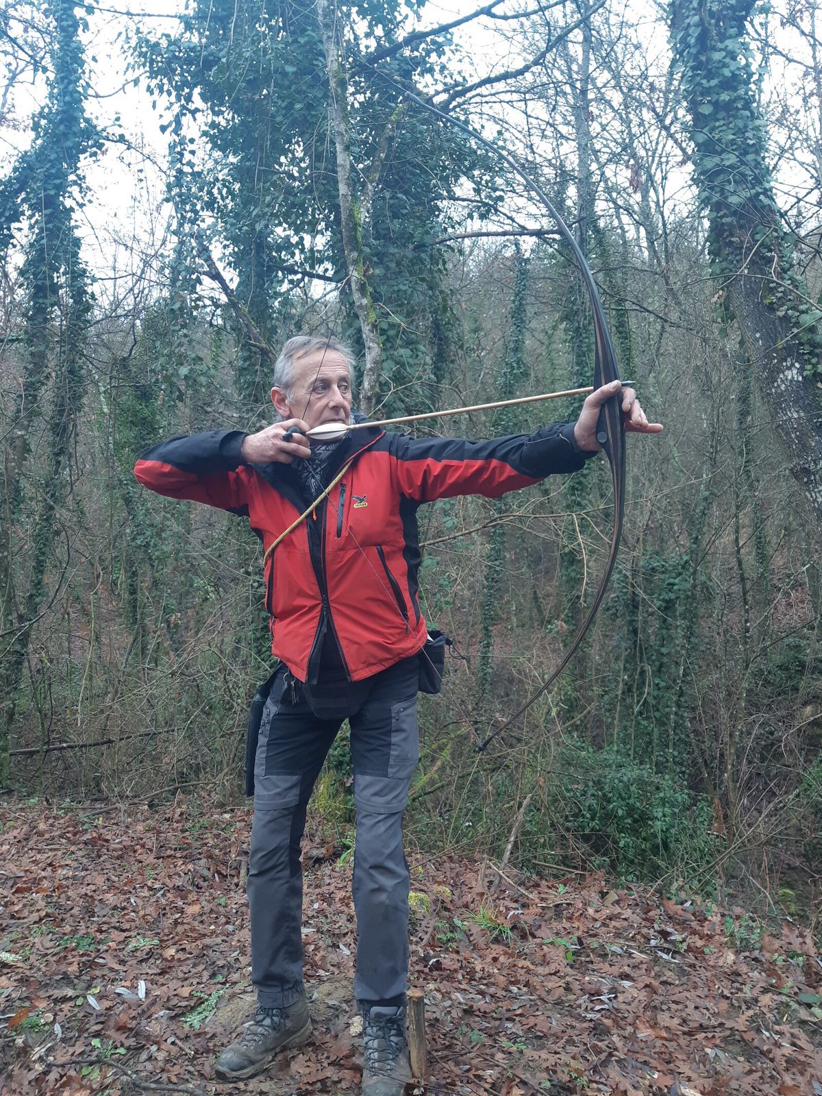 Langbogenschütze im Wald im Auszug, der Pfeil liegt auf der Bogenhand