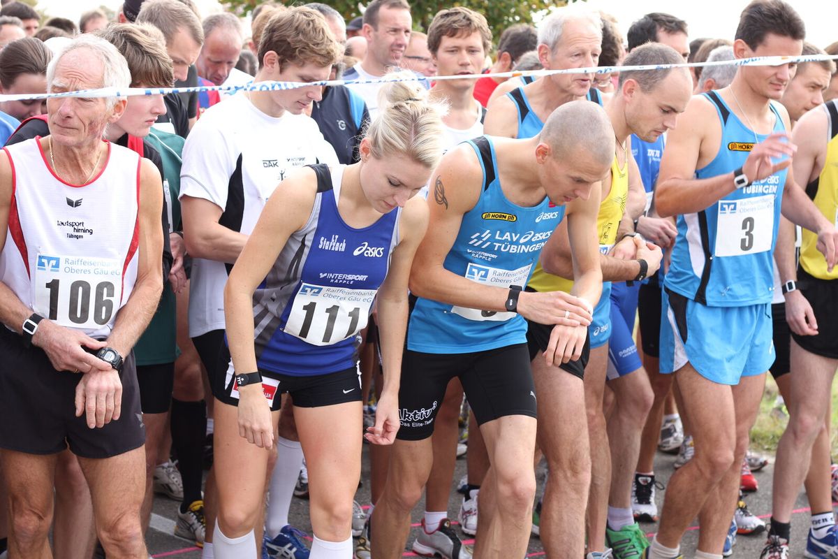 Zwei Sommerbiathleten mit Startnummern laufen über eine Wiesenstrecke