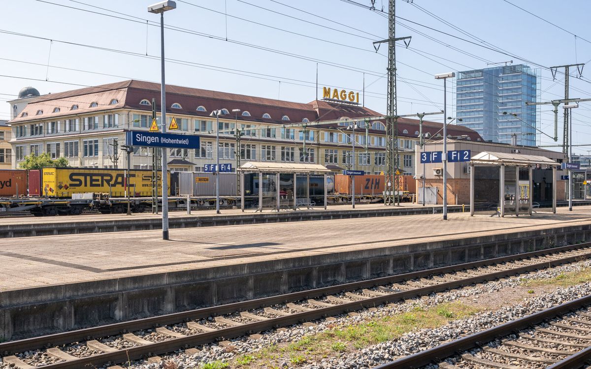 Bahnsteig im Bahnhof Singen (Hohentwiel) mit Stationsschild und Werksgebäude im Hintergrund