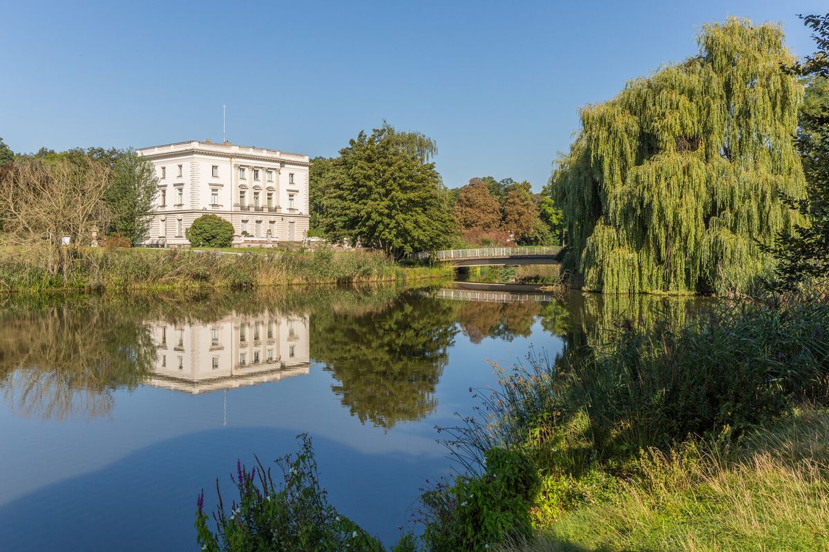 Das Weiße Haus im agra-Park Markkleeberg spiegelt sich in einem Parkteich, umgeben von Trauerweiden
