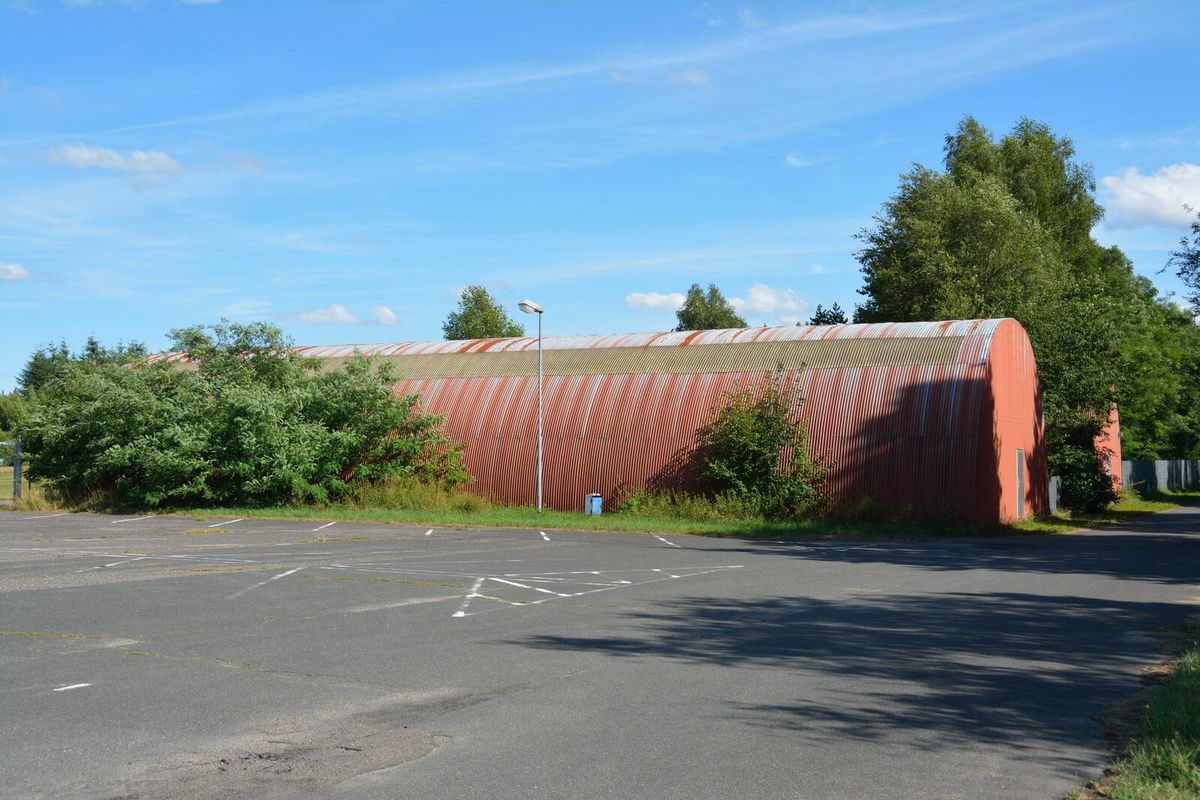 Leere asphaltierte Stellfläche mit aufgemalten Parkbuchten vor einer roten Hallentonne auf dem Flugplatz Hartenholm